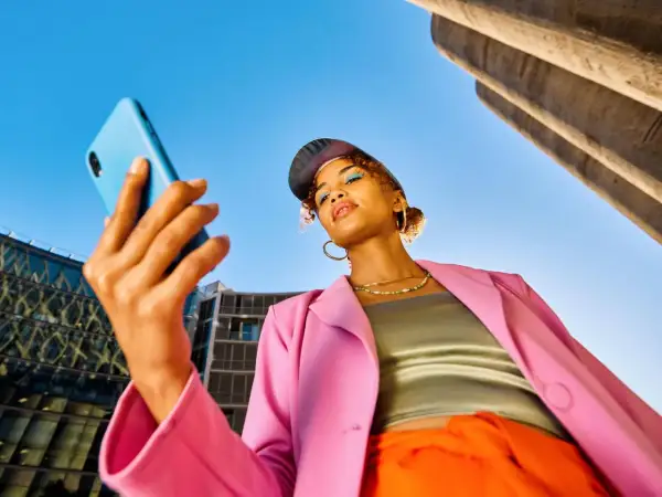 Junge Frau mit Handy in der Hand, blickt nachdenklich. Ist Influencer ein Beruf? Sie inspiriert mit ihrem Style.